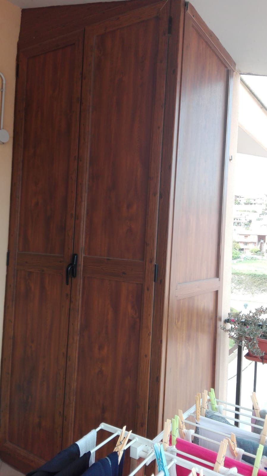 Armadio in metallo effetto legno su un portico; biancheria stesa ad asciugare sotto.