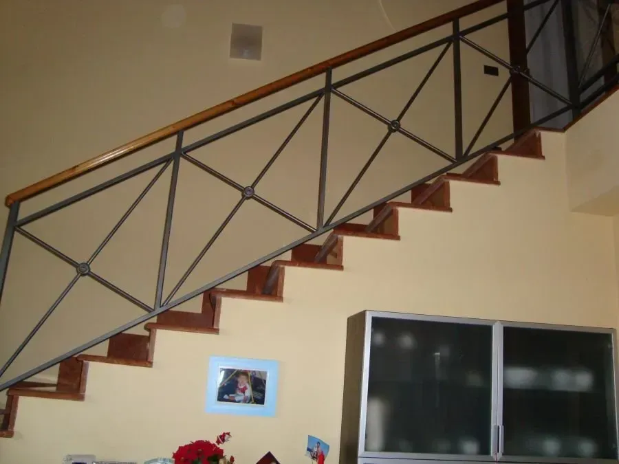 Scala in legno con ringhiera in metallo; pareti color crema, TV scura e foto incorniciata in vista.