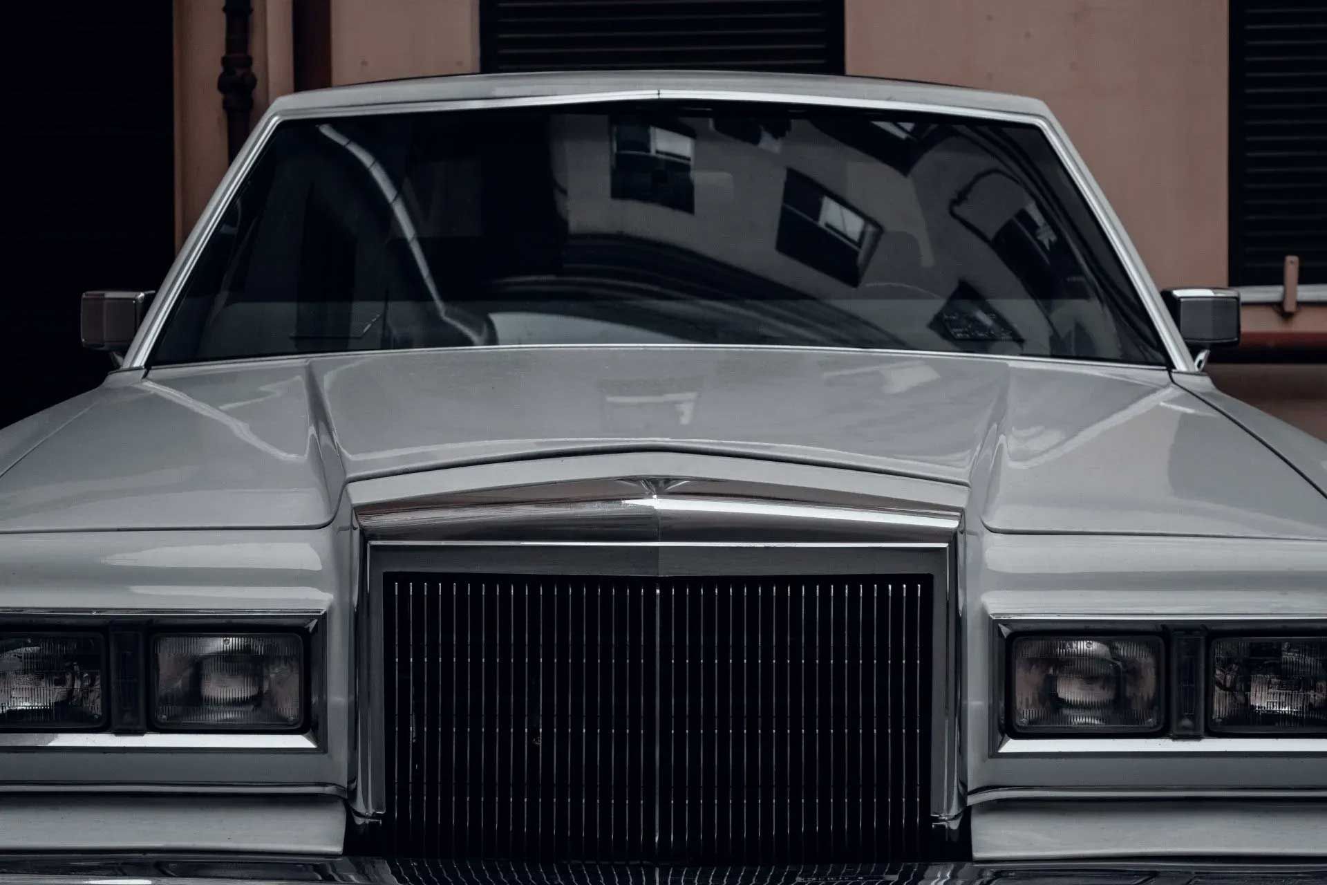 White vintage sedan parked outside building, with black grill and reflective windshield.