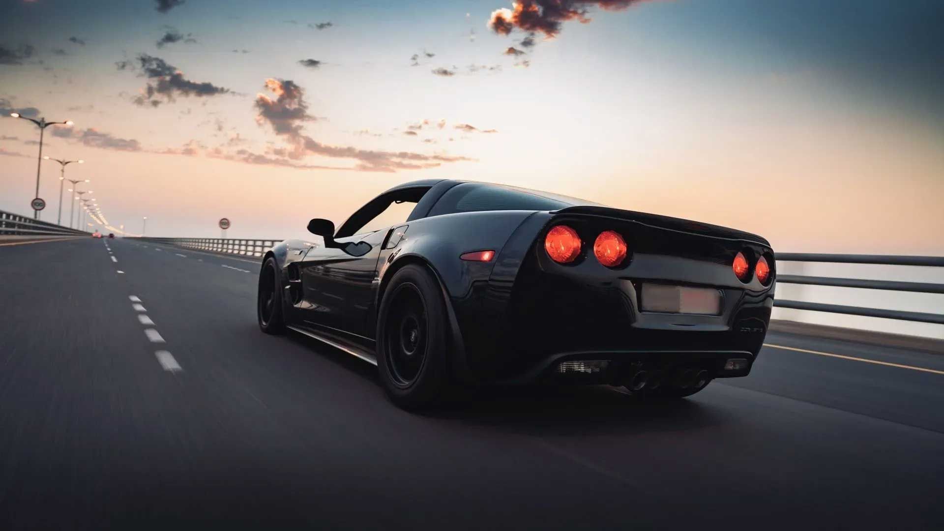 Black sports car driving on a bridge at sunset.