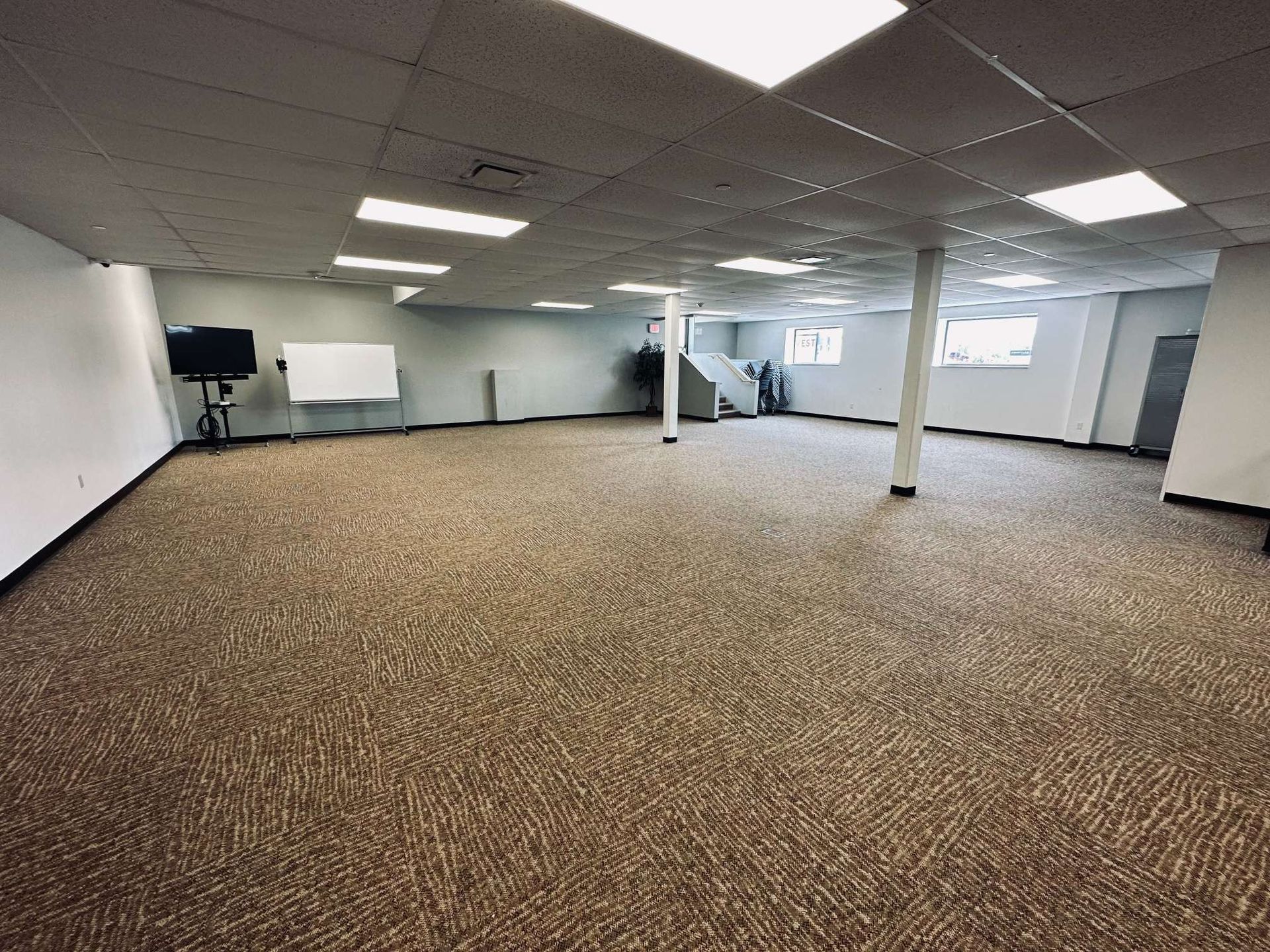 An empty room with a carpeted floor and a white board on the wall.