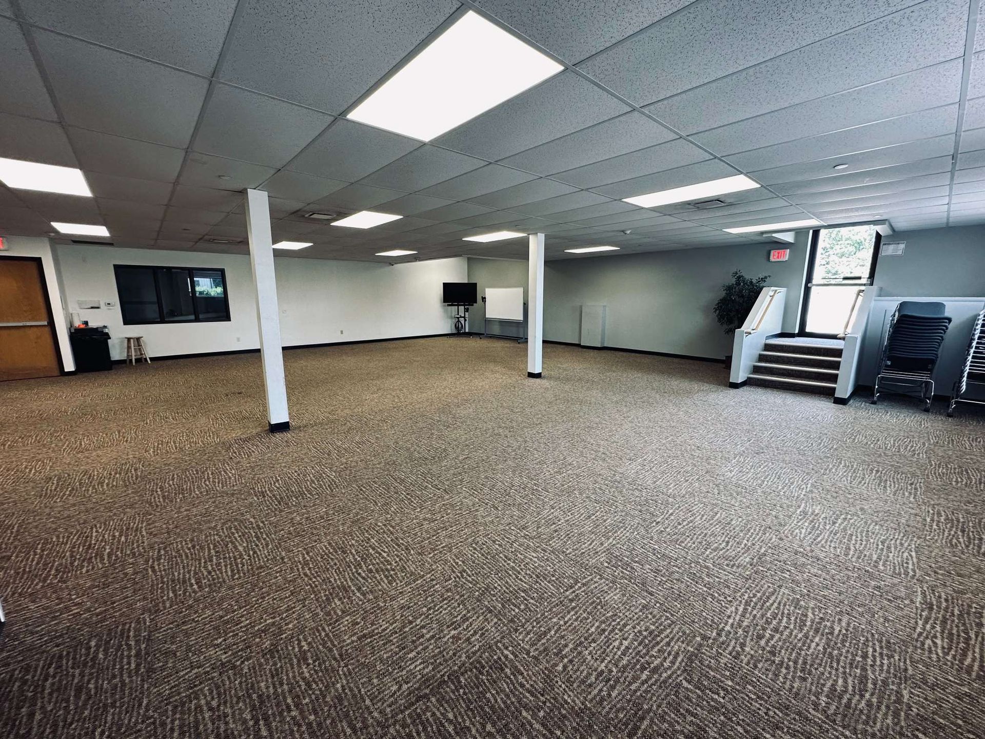A large empty room with a carpeted floor and stairs.