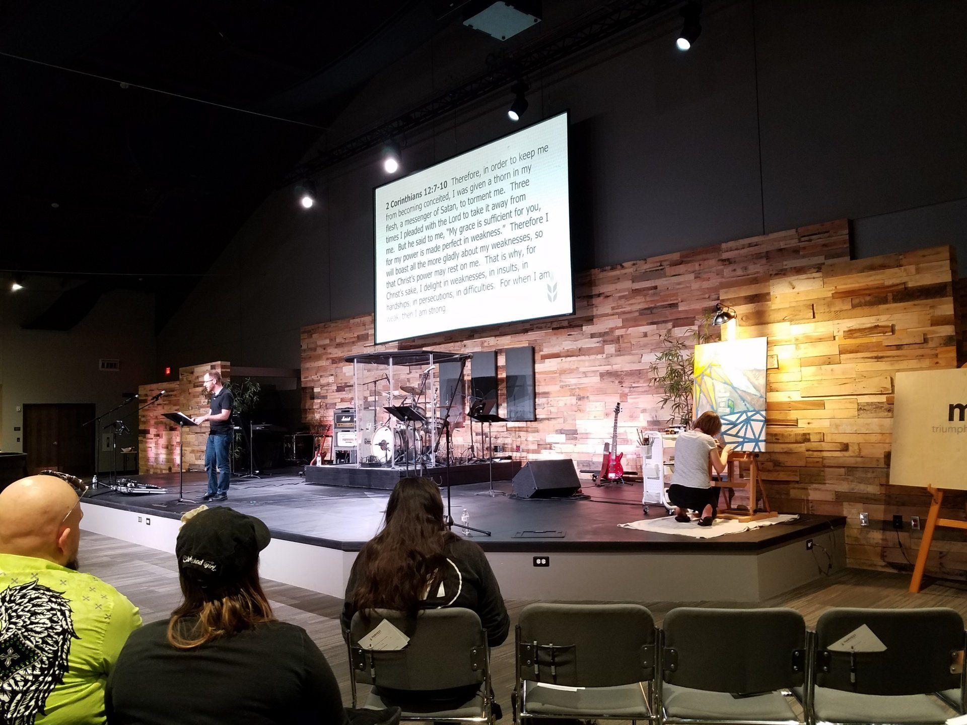 A group of people are sitting in chairs in front of a stage in a church.