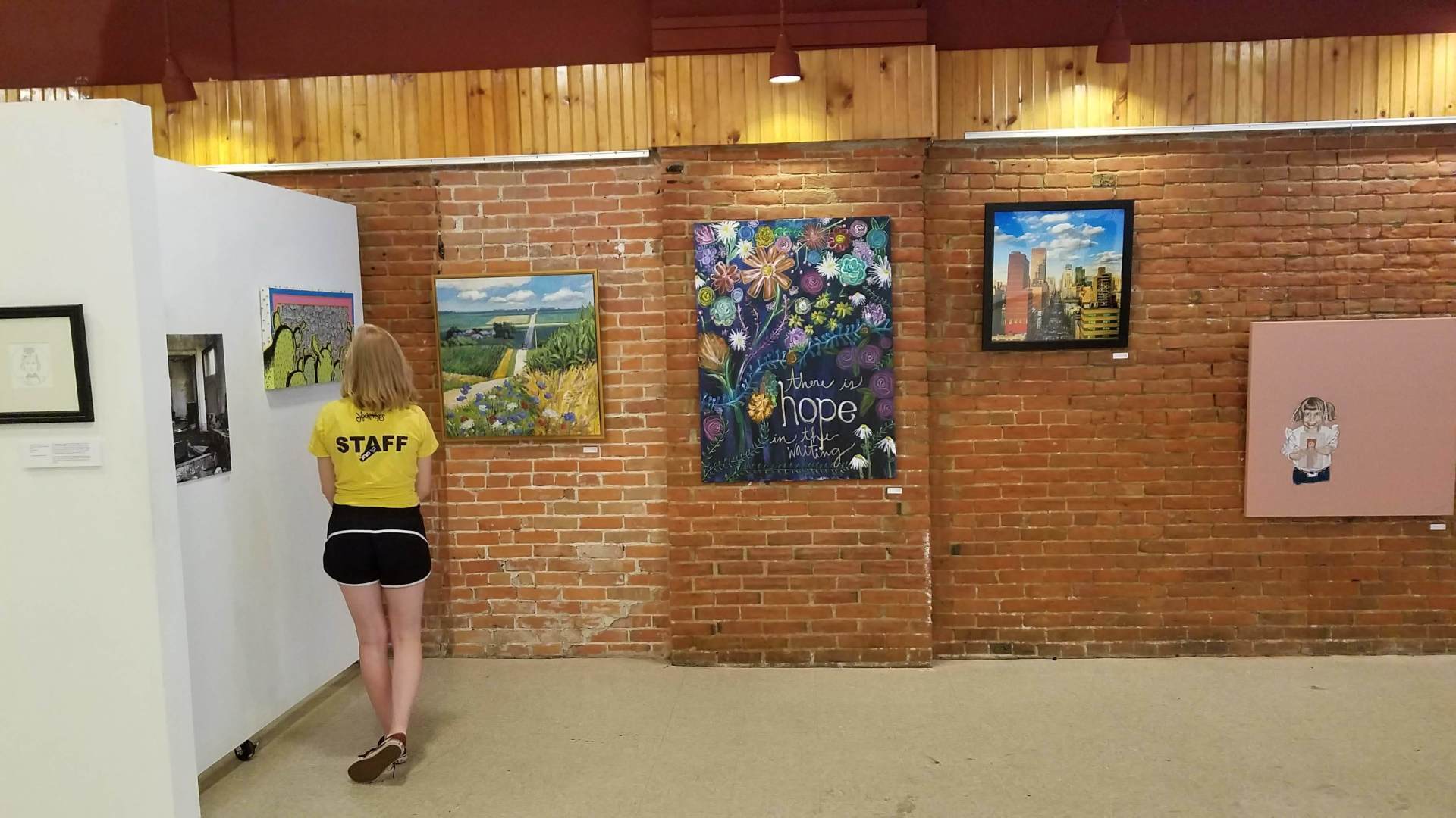 A woman in a yellow shirt is looking at paintings in a museum.