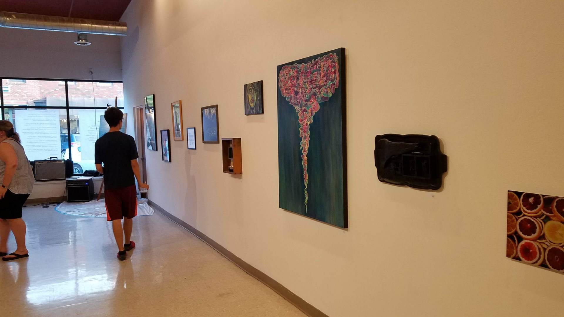 A man and a woman are walking down a hallway looking at paintings on the wall.
