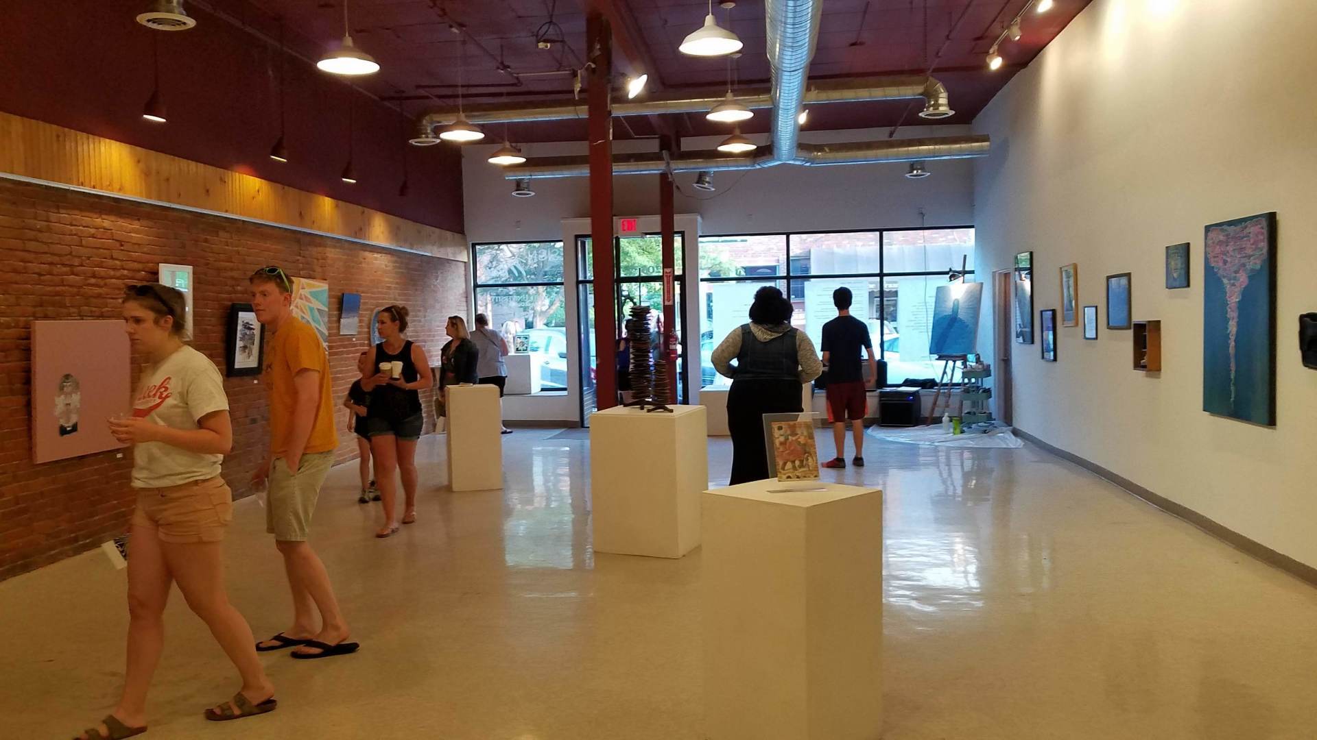 A group of people are standing in a large room looking at paintings.