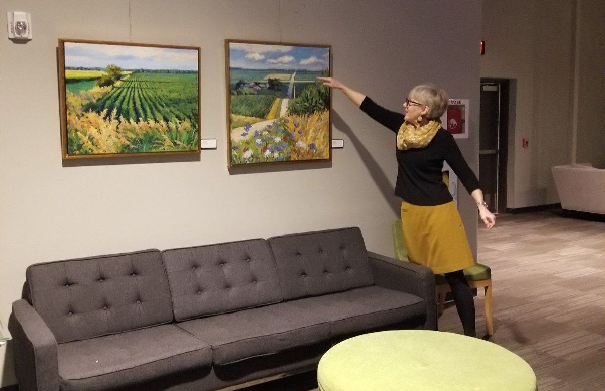 A woman is pointing at two paintings on a wall in a living room.