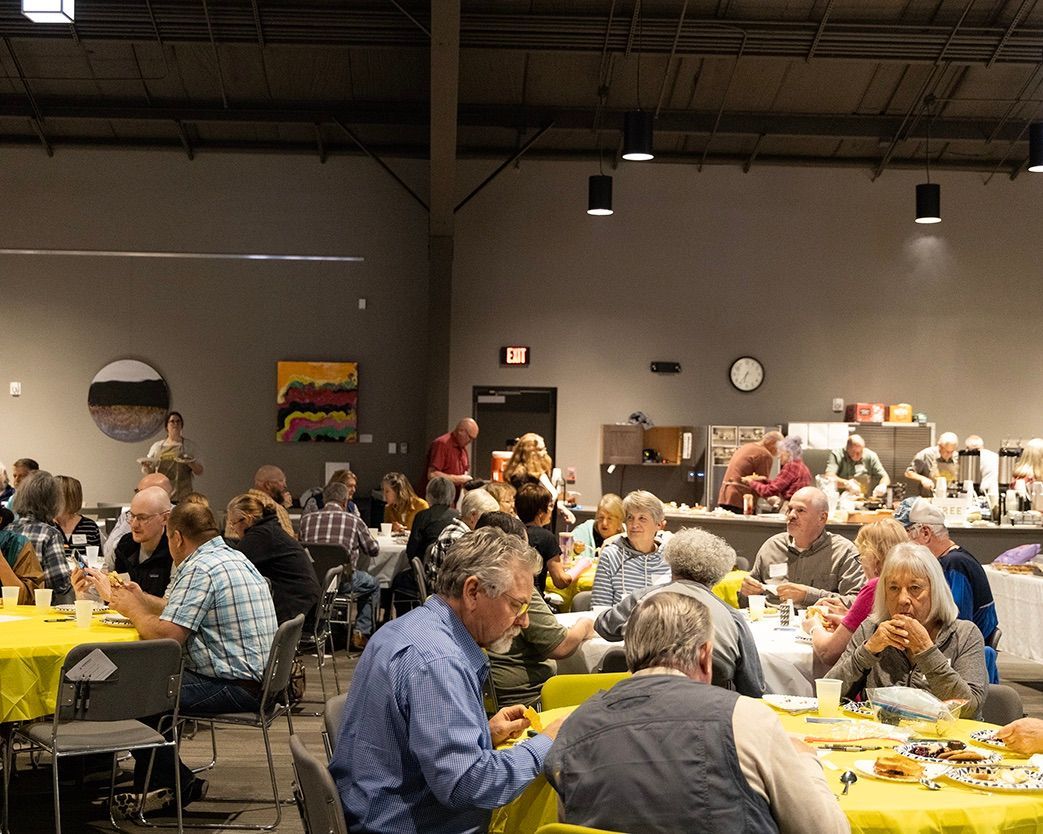 A large group of people are sitting at tables in a large room eating food.