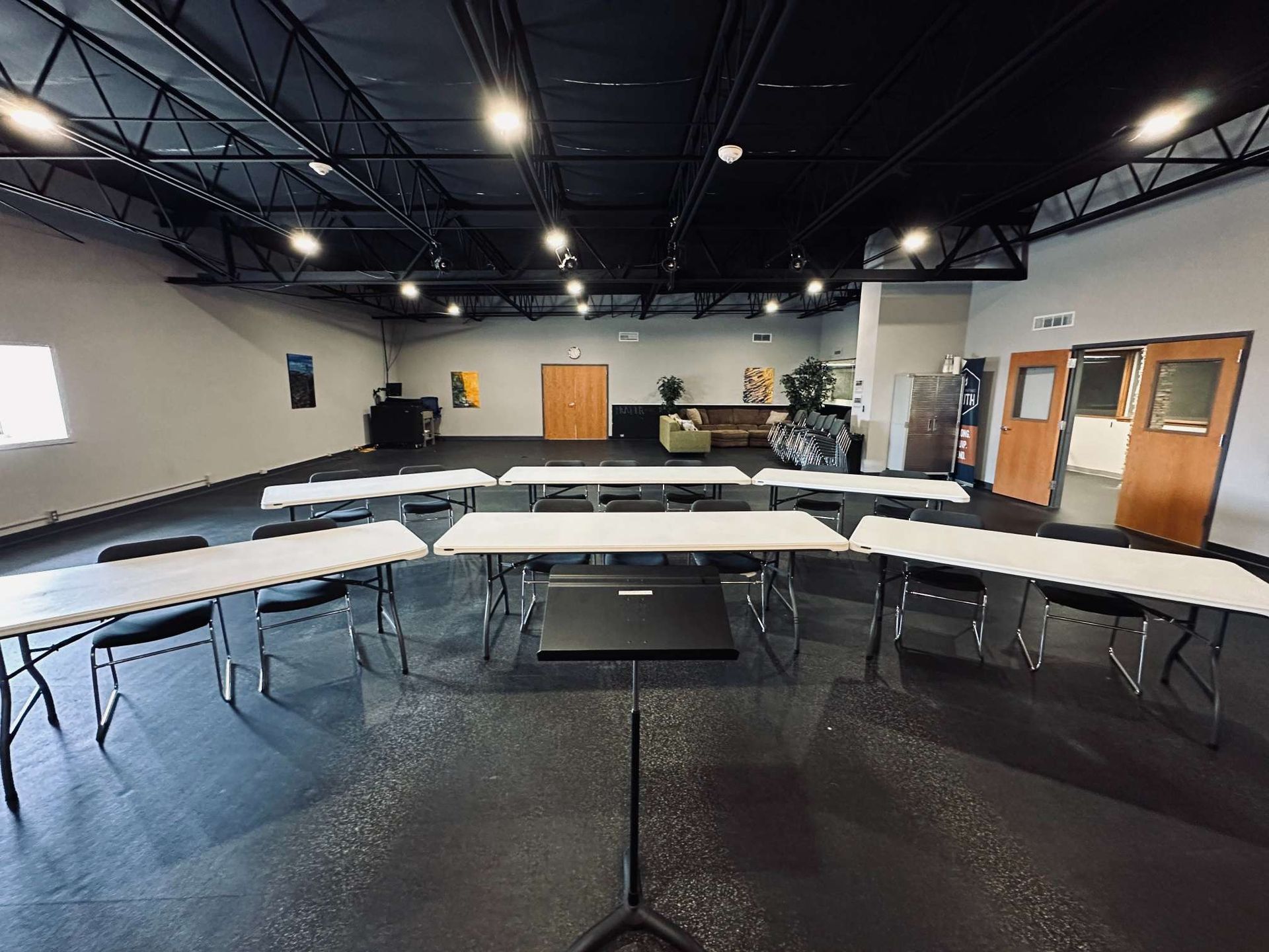 A large room with tables and chairs and a laptop on a stand.