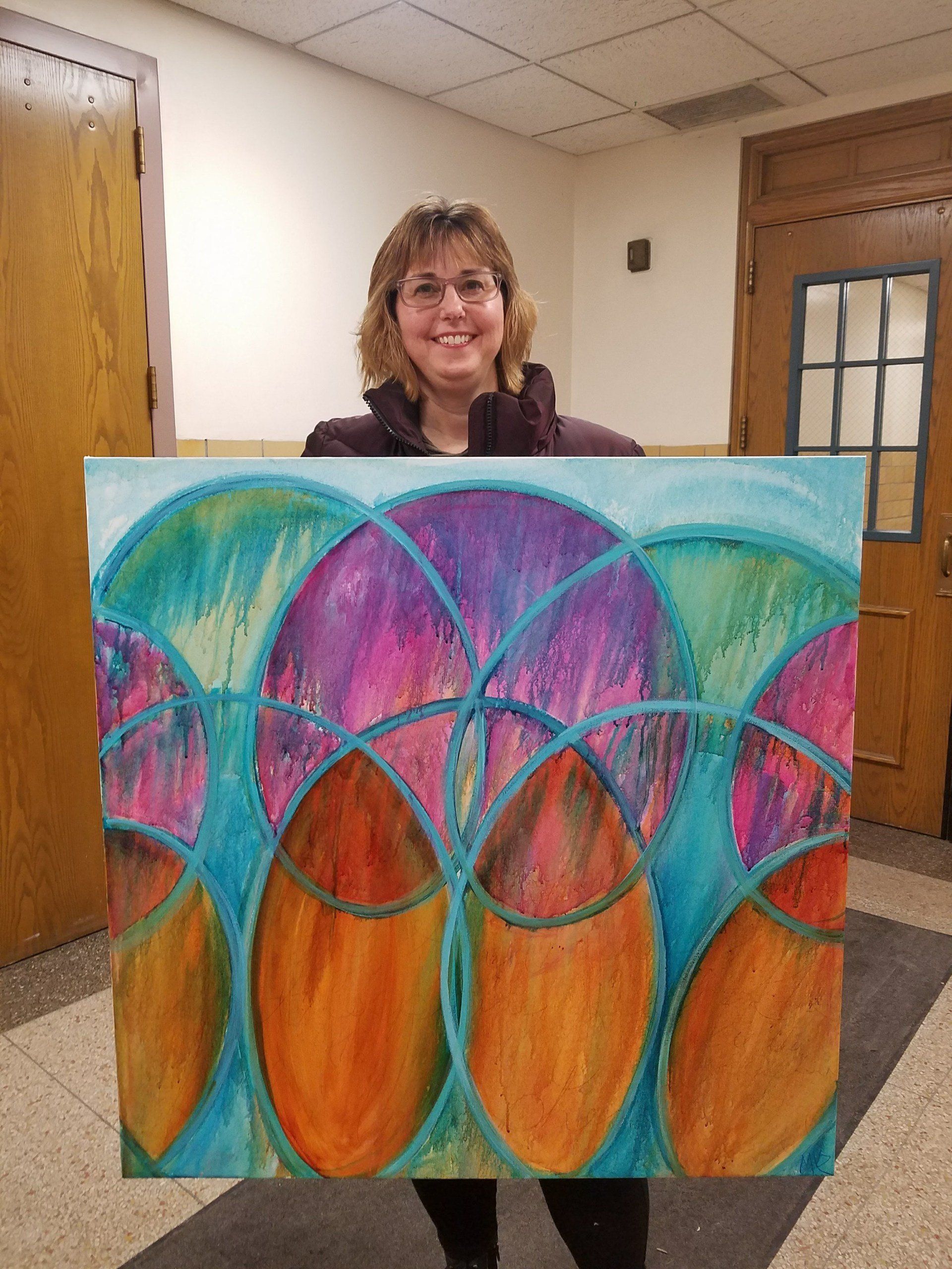 A woman is holding a colorful painting in her hands.
