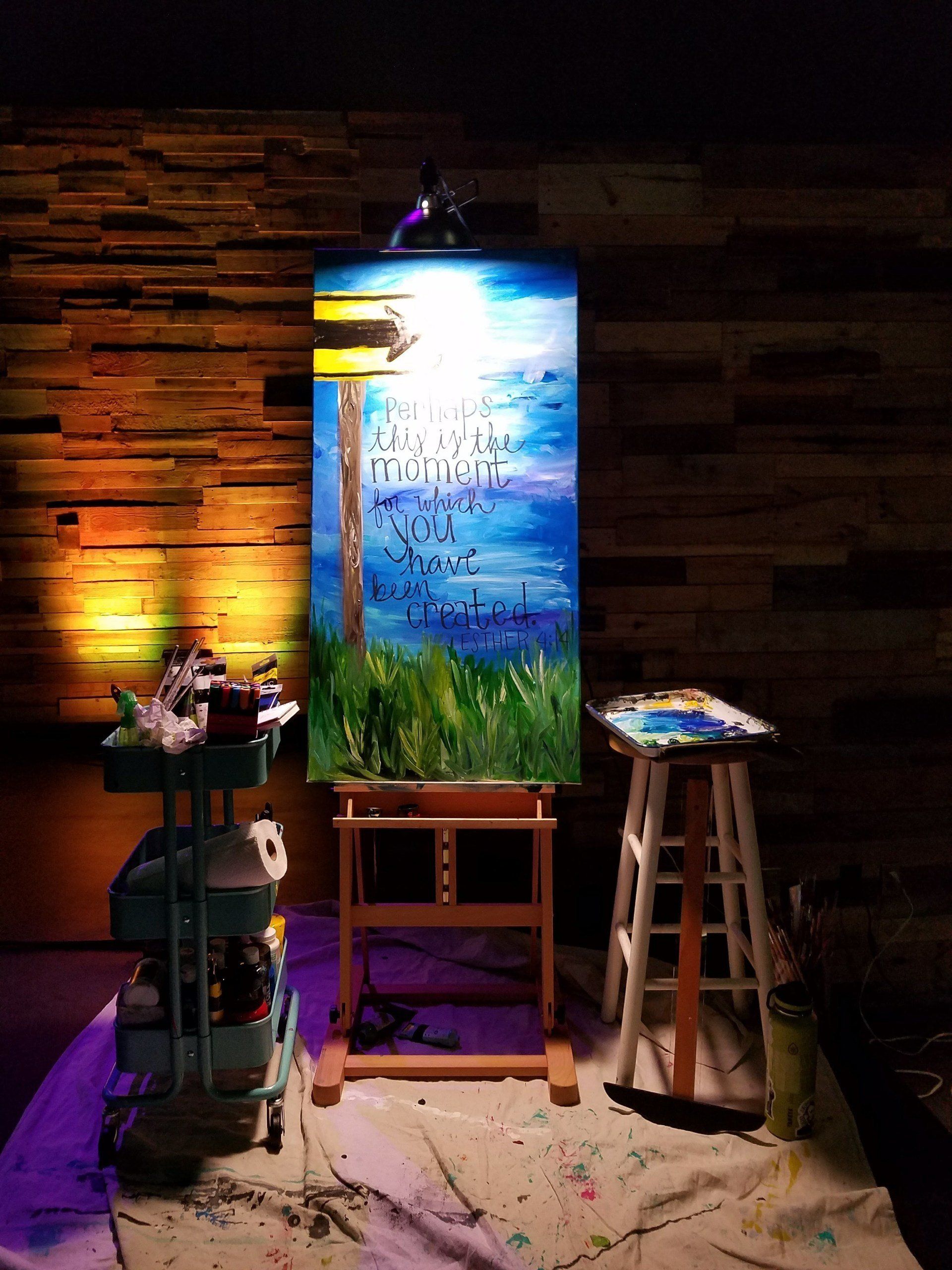 A large painting is on an easel in a dark room.