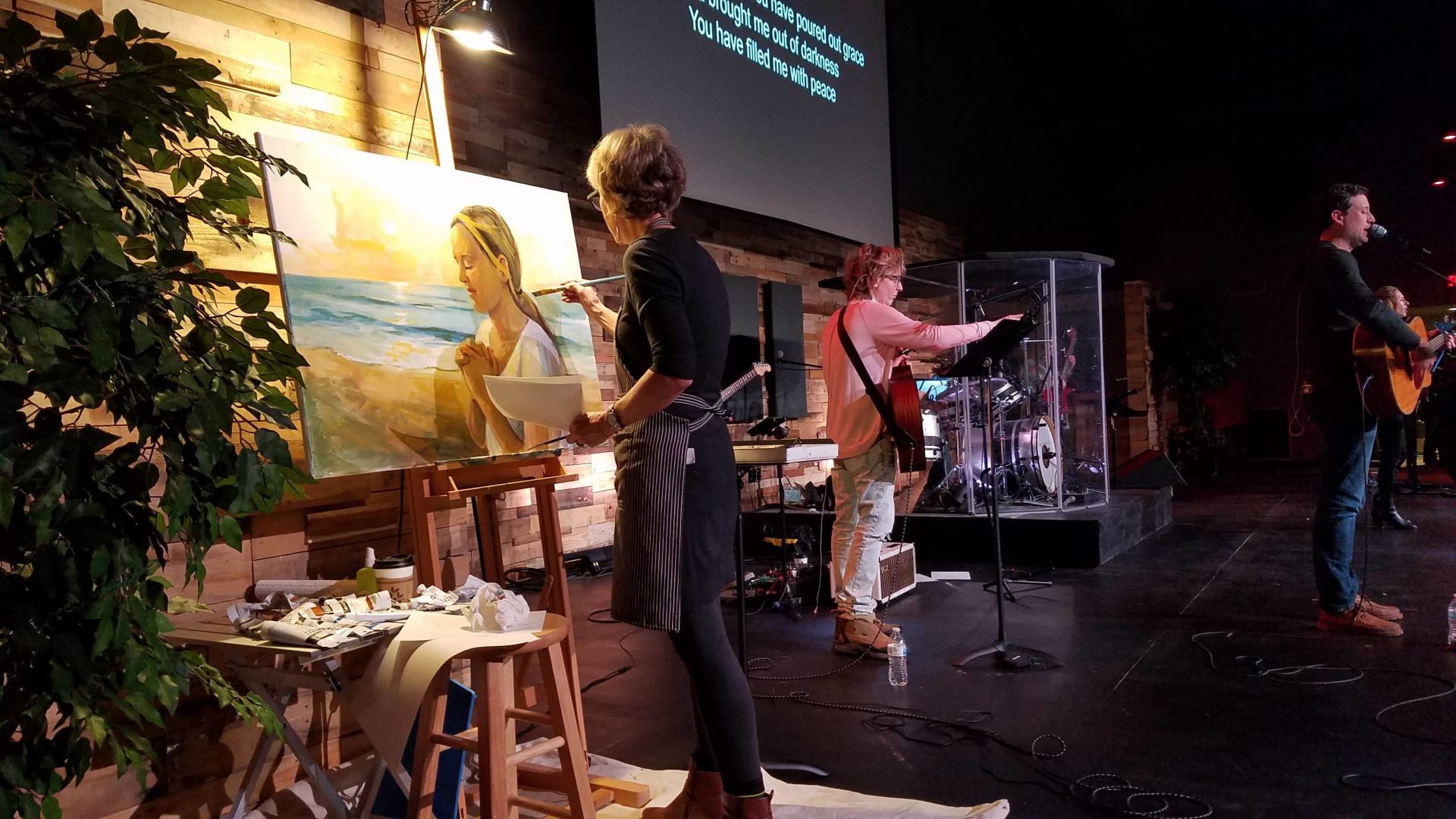 A group of people are standing on a stage painting a picture.