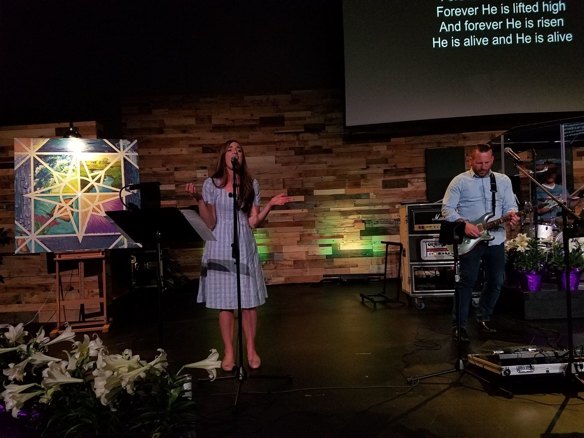 A woman is singing into a microphone on a stage while a man plays a guitar.