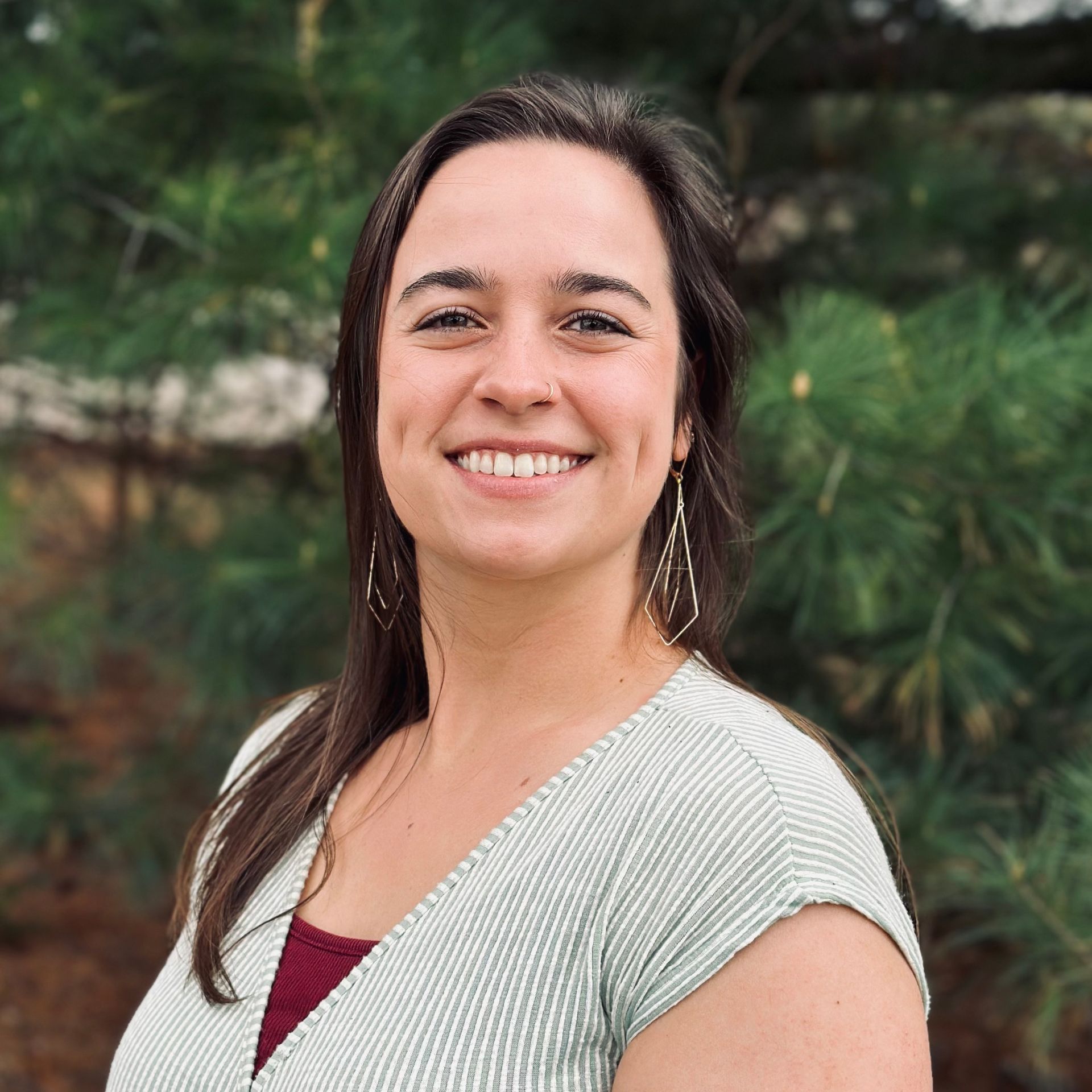 A woman is smiling for the camera in front of a pine tree.