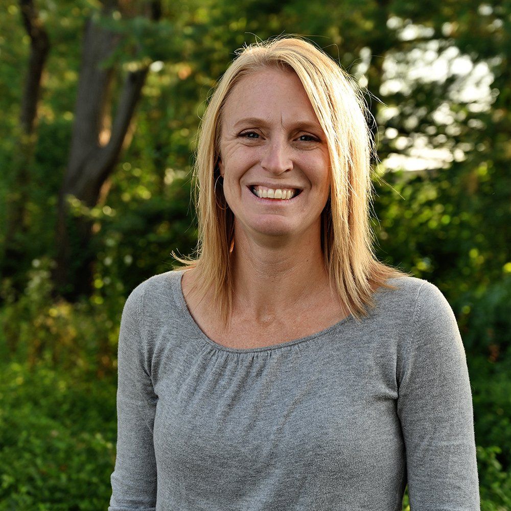 A woman in a grey shirt is smiling for the camera