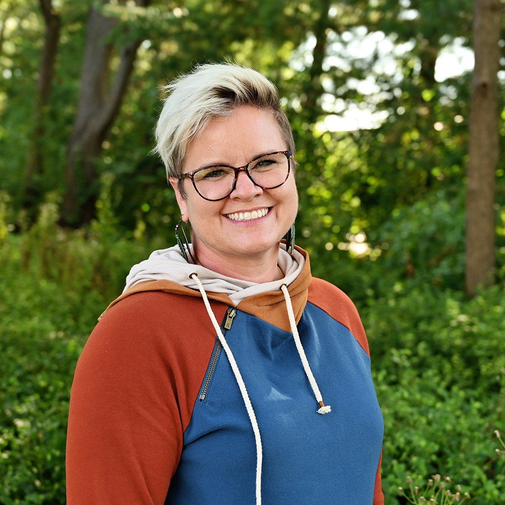 A woman wearing glasses and a hoodie is smiling for the camera.