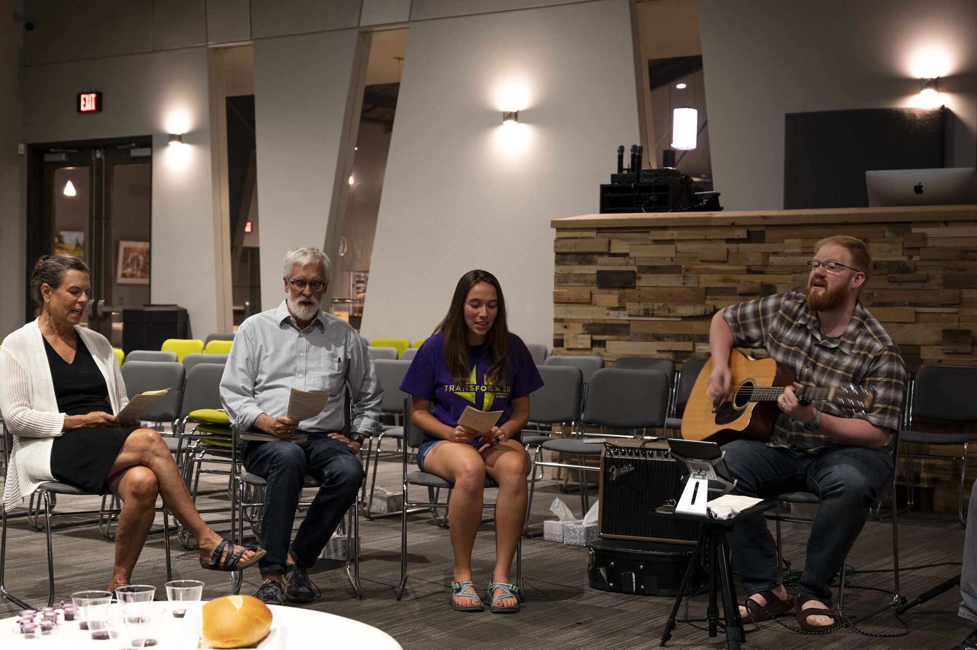 A group of people are sitting in chairs in a room while a man plays a guitar.