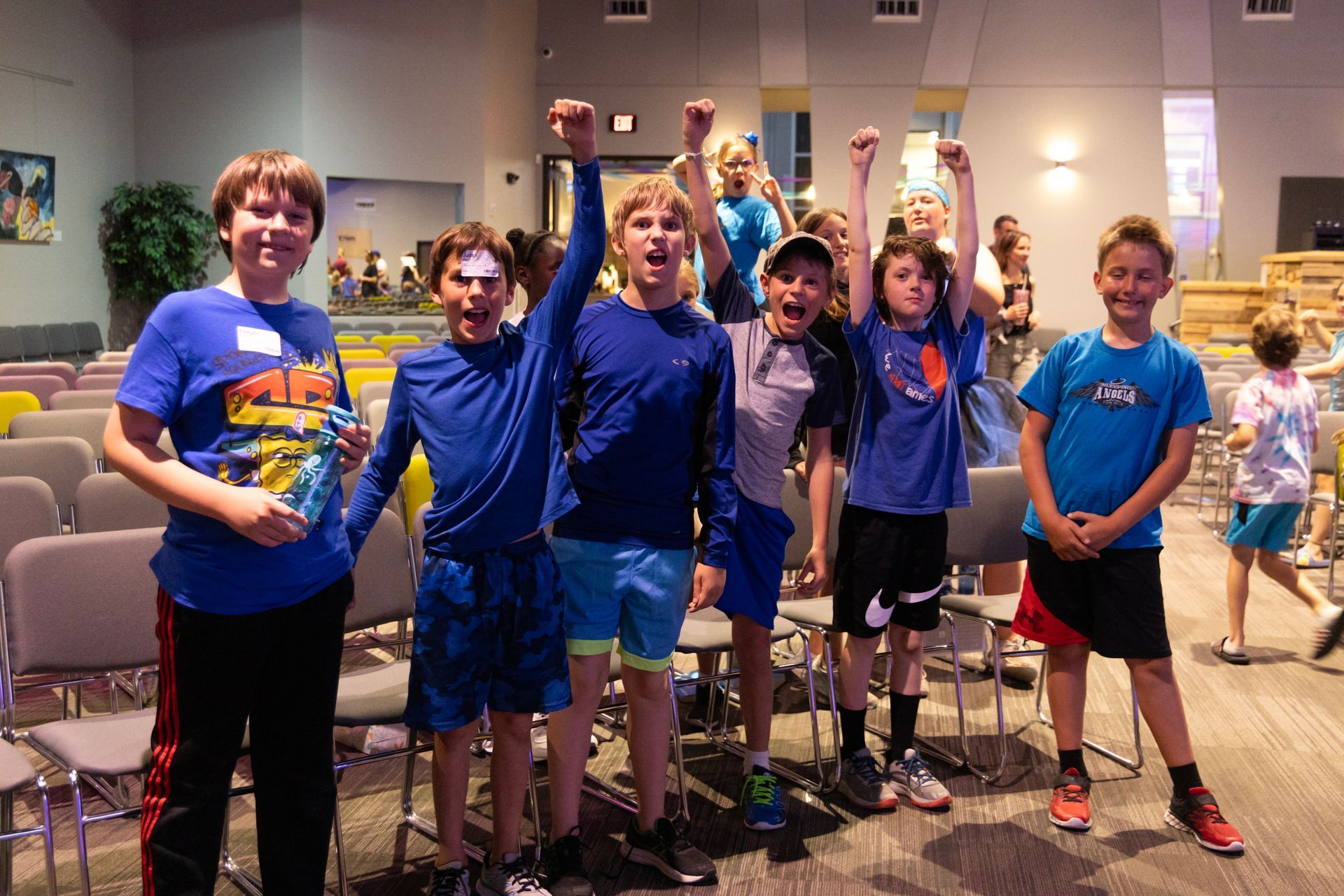 A group of young boys are standing in a room with their arms in the air.