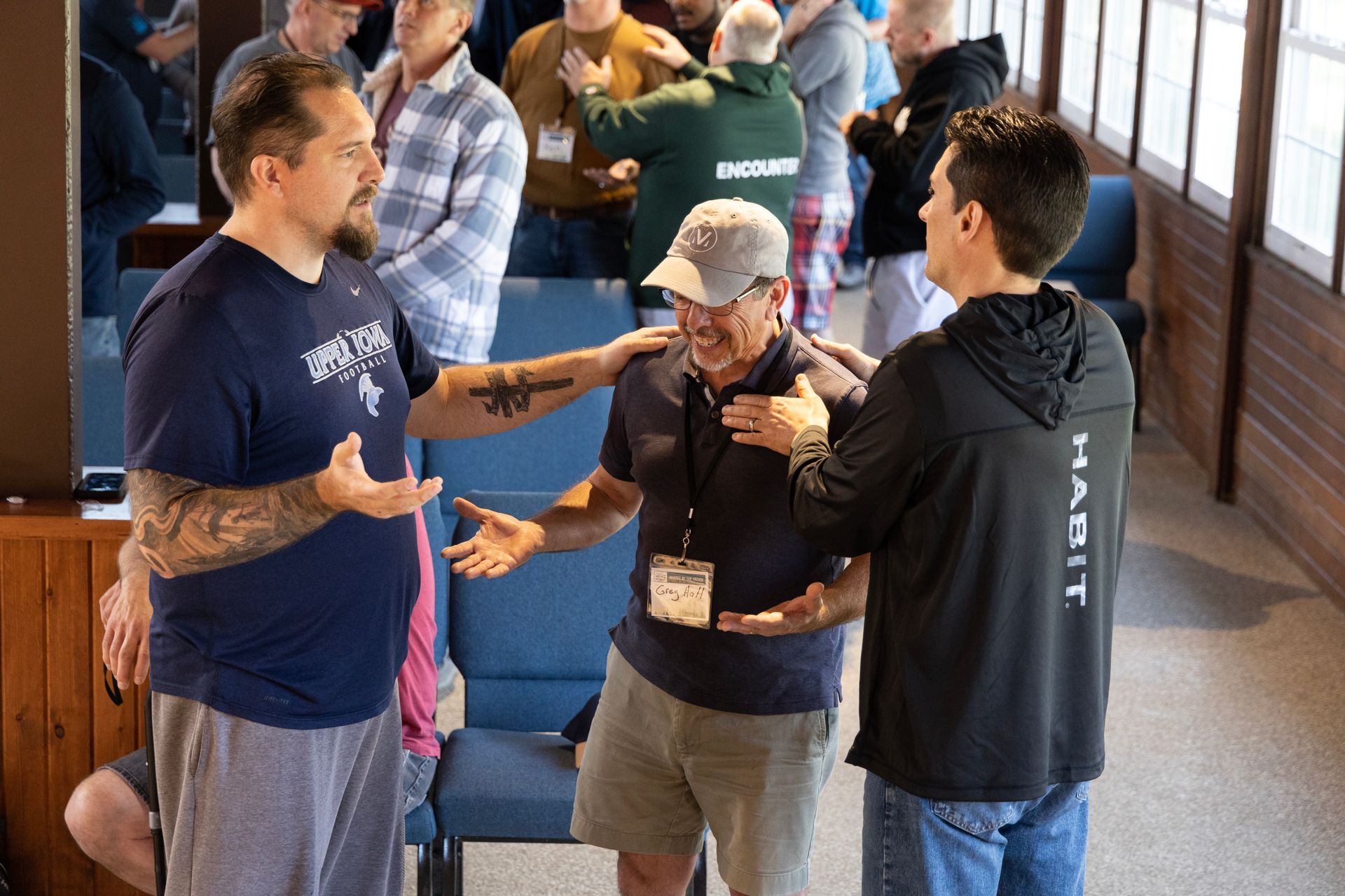 A group of men are standing in a room talking to each other.