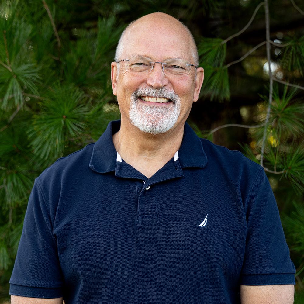 A man in a black shirt is standing in front of trees.