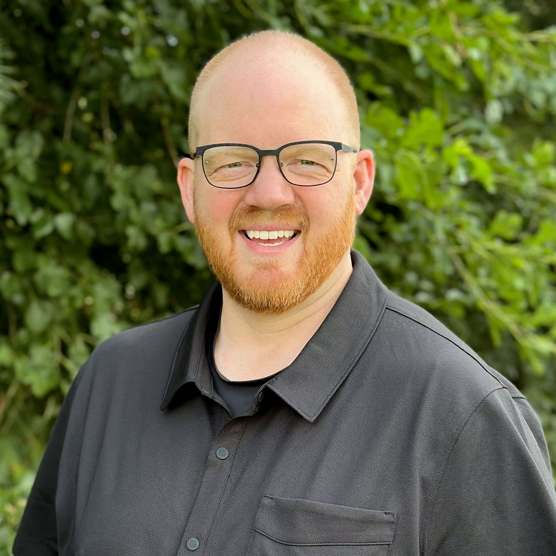 A man with a beard and glasses is smiling with his arms crossed.