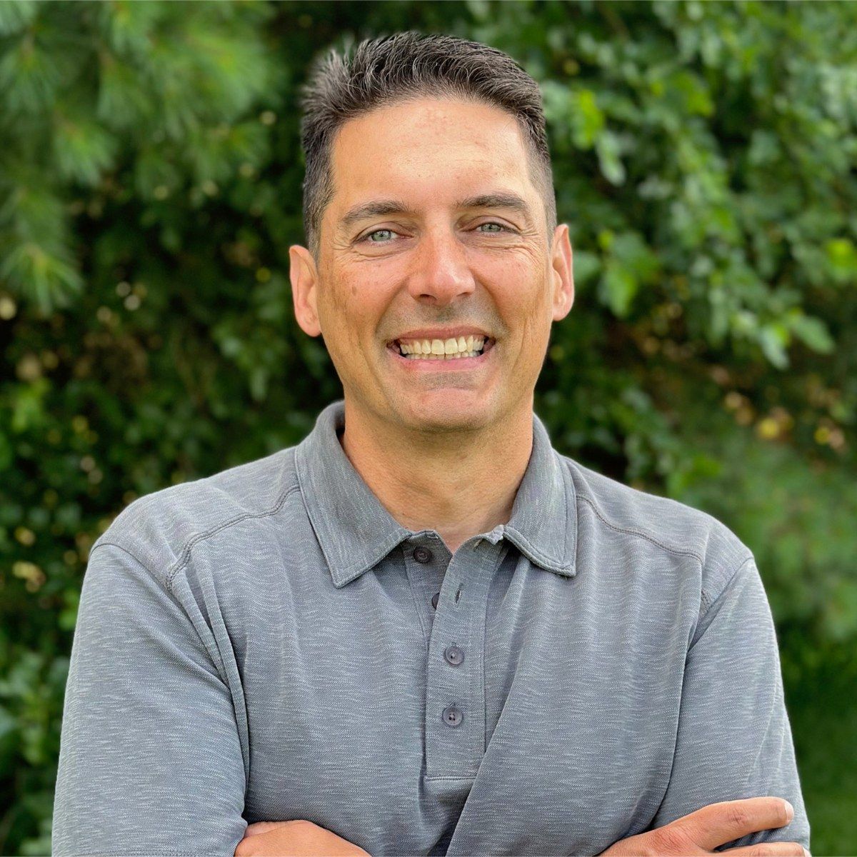 A man in a black shirt is standing in front of trees.