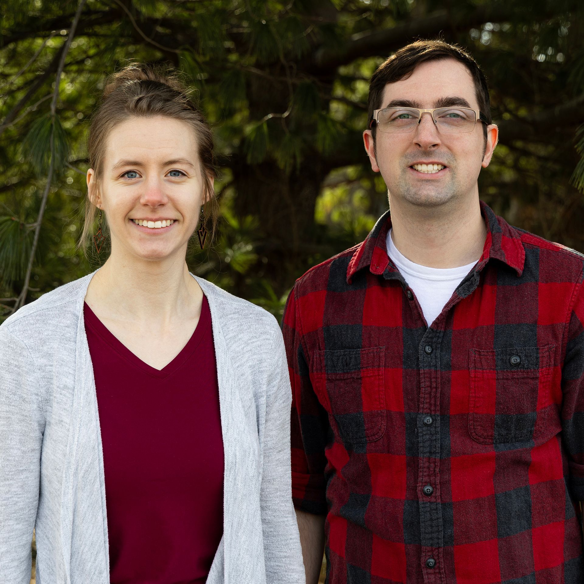 A man and a woman are posing for a picture in front of a pine tree.