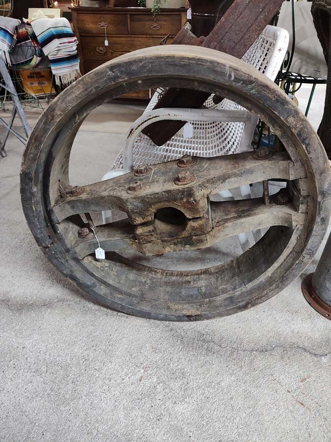 Large, weathered wooden wheel with metal accents on concrete floor.