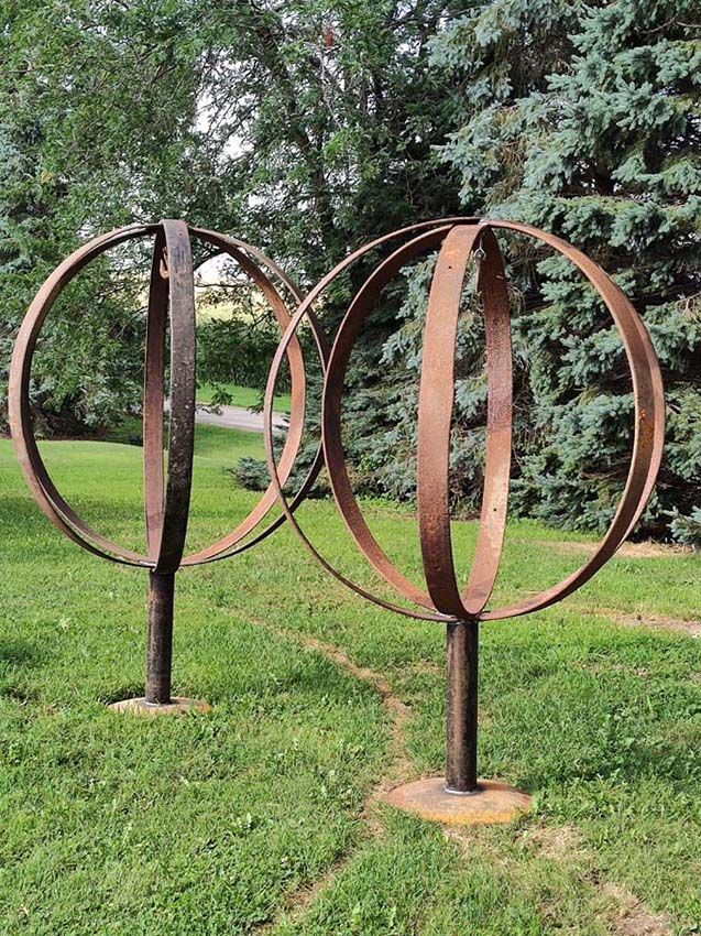 Two rusty metal spherical sculptures on posts in a grassy park, trees in background.