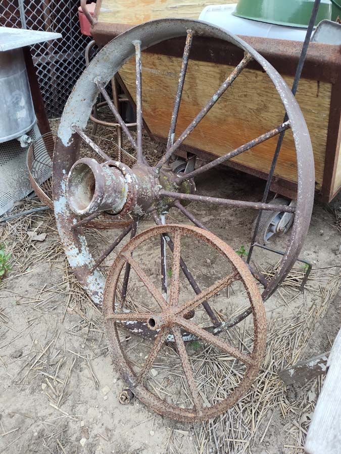Two weathered metal wagon wheels, one large, one small, rest outdoors.