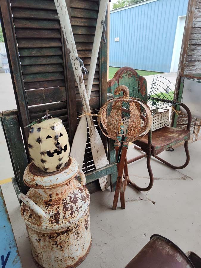 Rustic Halloween display: Rusty milk can with jack-o-lantern head, weathered chair, shutters, and antique yard decor.
