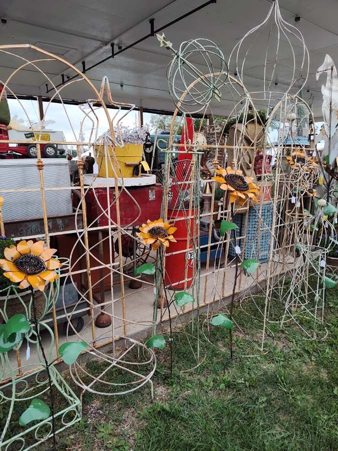 Metal garden trellises with attached artificial sunflowers on display at an outdoor market.