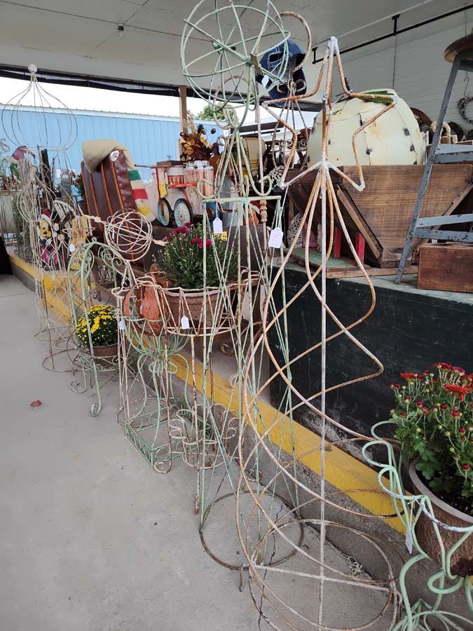 Metal plant stands, in various shapes, are displayed outside. Some hold flowers.