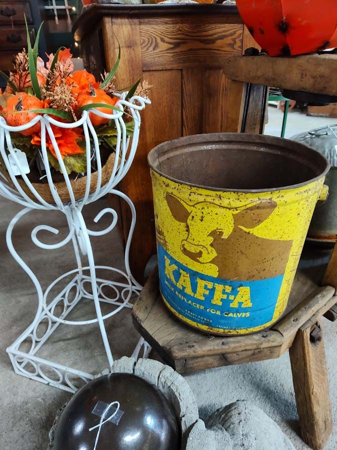Yellow and blue Kaffa tin on a wooden stool, white floral stand with pumpkins, and a dark sphere.