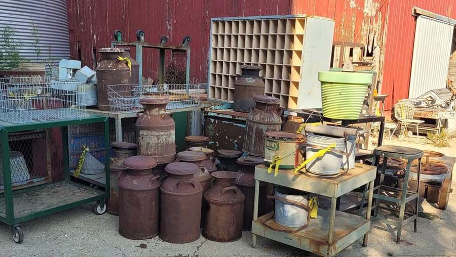 Pile of rusty metal milk cans and other vintage items for sale in a yard.
