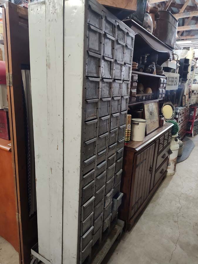 Tall, white and gray metal cabinet with many small drawers in a cluttered room.