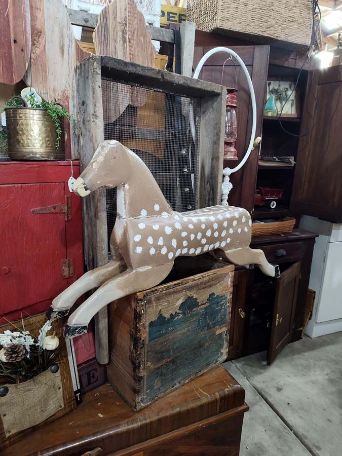 Wooden horse with white spots, displayed atop a trunk, in an antique shop.