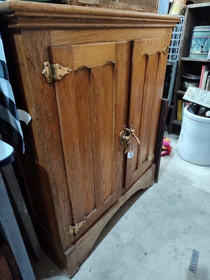 Wooden cabinet with two doors, brass hardware, sitting on concrete floor.