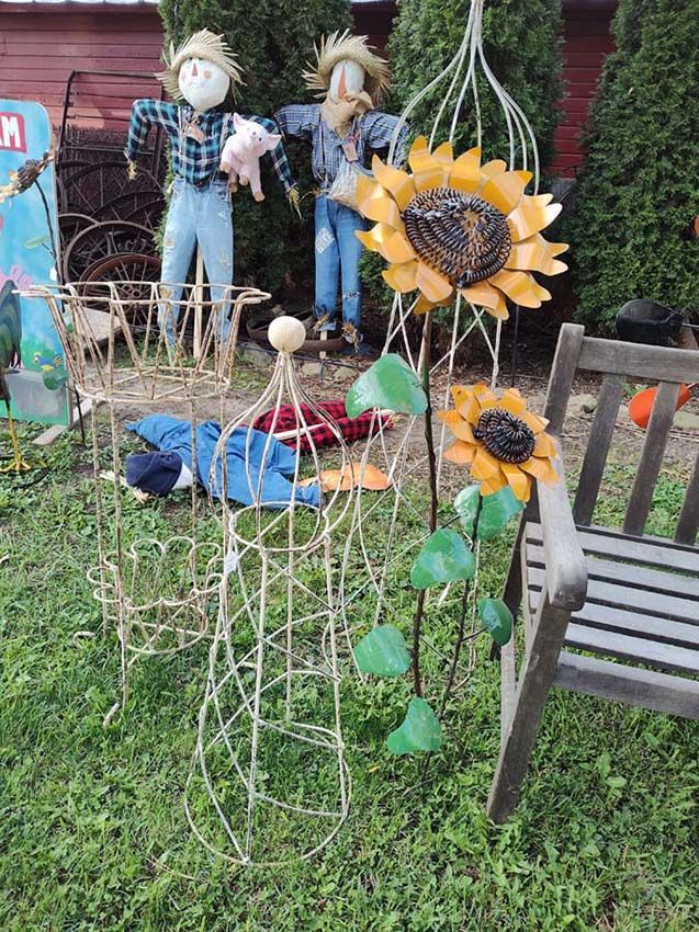 Yard display with scarecrows, metal sunflowers, and a wooden bench on green grass.