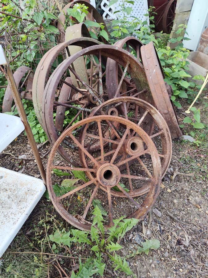 Rusty wagon wheels piled in overgrown grass.