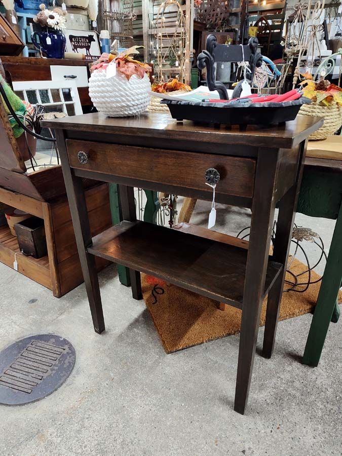 Wooden brown side table with a drawer and shelf. A basket sits on top.