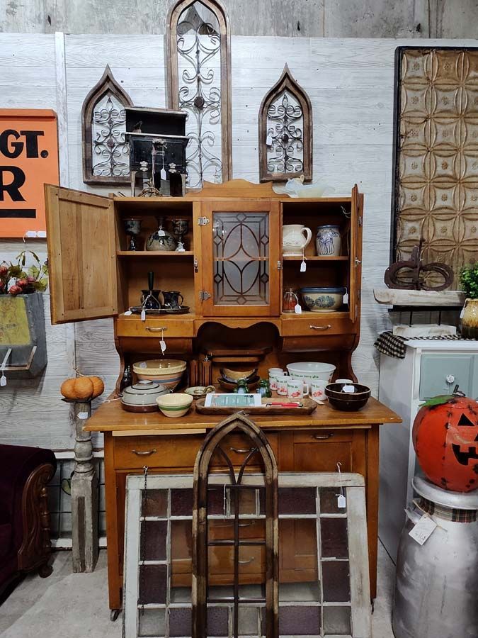 Antique wooden hutch with open doors, displaying vintage items.  Arched decor on wall, pumpkins nearby.