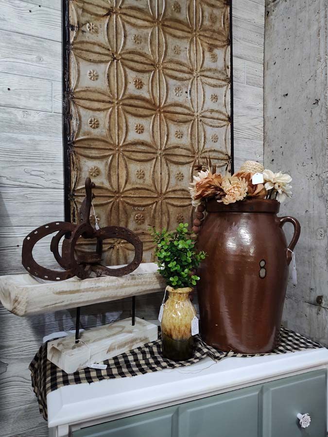 Brown and tan decor arrangement: a large jug with flowers, horseshoe art, and a decorative tin panel.