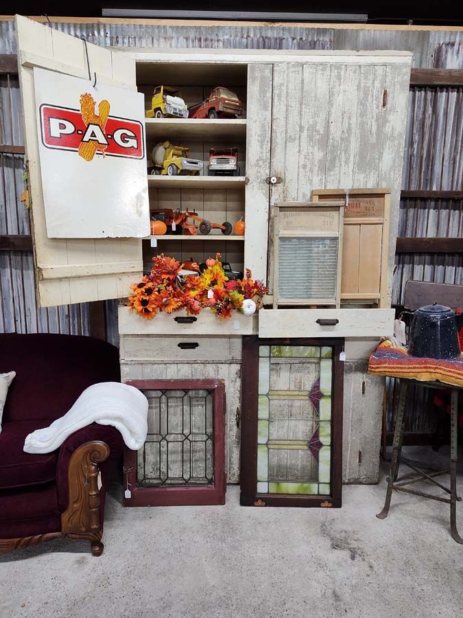 Antique white cabinet with open doors, fall decor, toy trucks, stained glass windows.