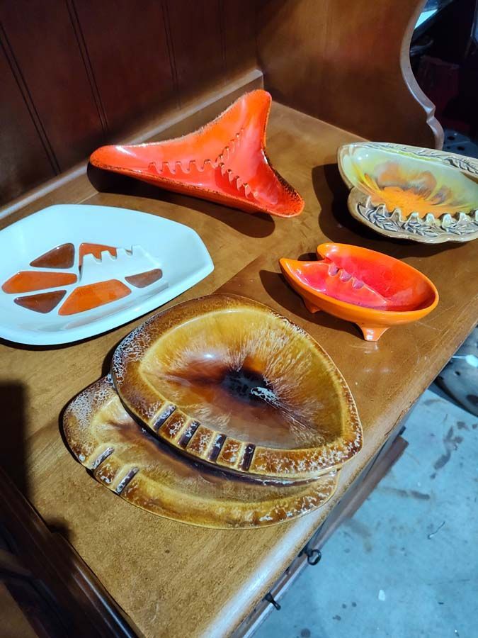 Mid-century ashtrays in orange, brown, and yellow on a wooden surface.