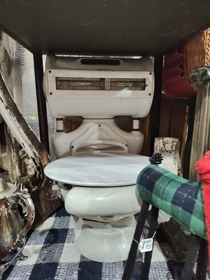 White antique scale, circular top, under a shelf, sitting on a blue and white checkered rug.