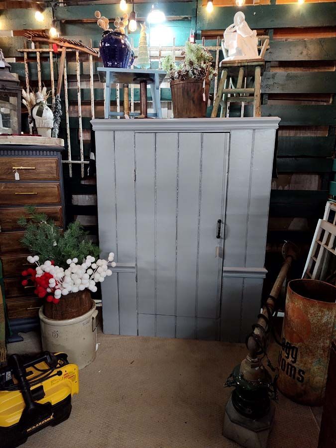 Gray wooden cabinet with a single door, surrounded by various antiques.