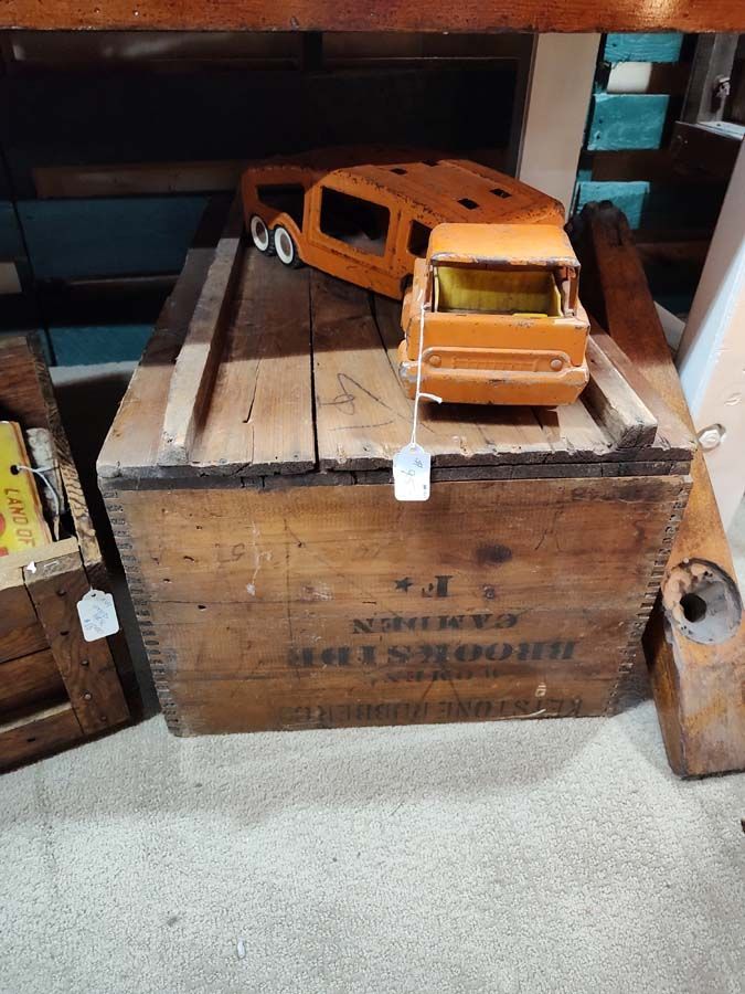 Orange toy truck and trailer on a wooden crate with text, in a shop setting.