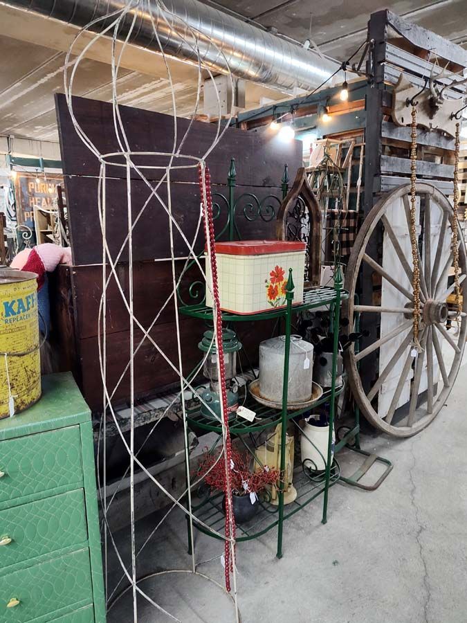 Assortment of antique items in a shop: cart wheel, metal plant stand, decorative wire frame, old storage tin.