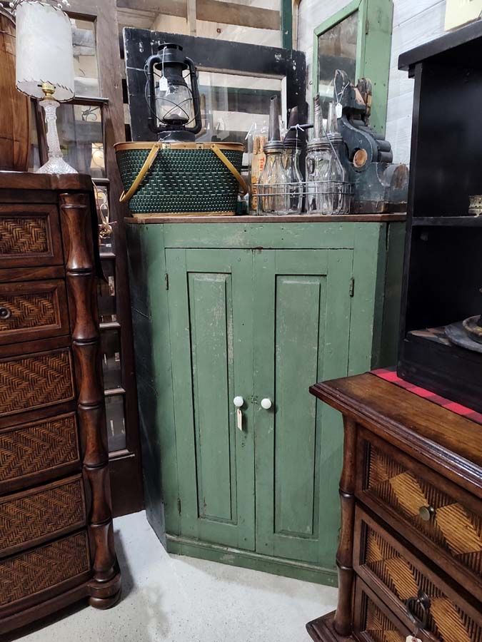 Green corner cabinet with vintage items on top, in a shop.